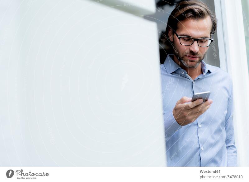 Mann steht im Türrahmen und benutzt ein Mobiltelefon Tuerrahmen stehen stehend Handy Handies Handys Mobiltelefone halten Männer männlich Geschäftsmann