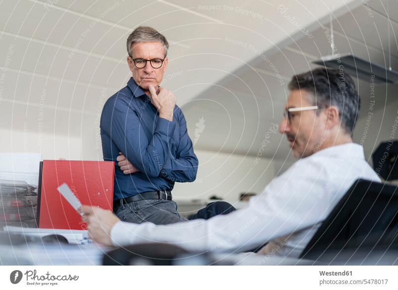 Ältere männliche Mitarbeiter diskutieren über ein Dokument, während sie im Büro sitzen Farbaufnahme Farbe Farbfoto Farbphoto Deutschland Innenaufnahme