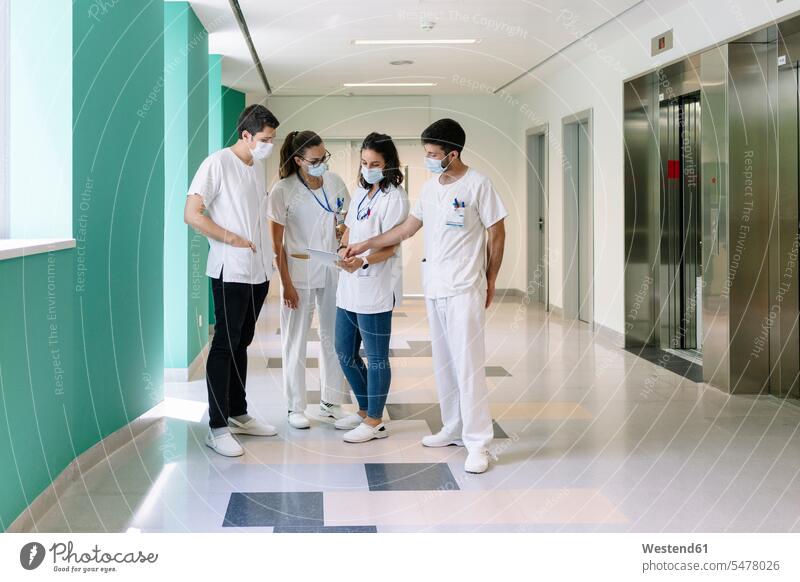 Ärzte mit chirurgischen Masken diskutieren über digitales Tablet, während sie im Krankenhaus auf dem Flur stehen Farbaufnahme Farbe Farbfoto Farbphoto Spanien