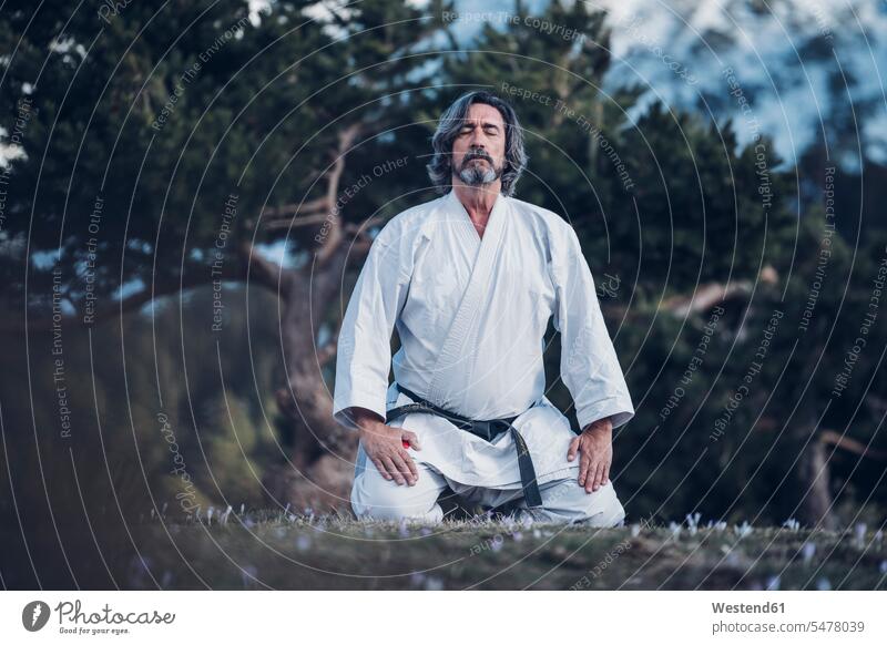 Senior Mann übt Karate im Freien, Meditation Männer männlich ältere Männer älterer Mann Senioren Karateka Karatekaempfer Karatekämpfer Karatekas sitzen sitzend