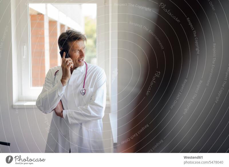 Arzt stehend im Krankenhaus, mit Smartphone Arztkittel iPhone Smartphones Stethoskop Stethoskope Doktoren Ärzte Portrait Porträts Portraits Kliniken