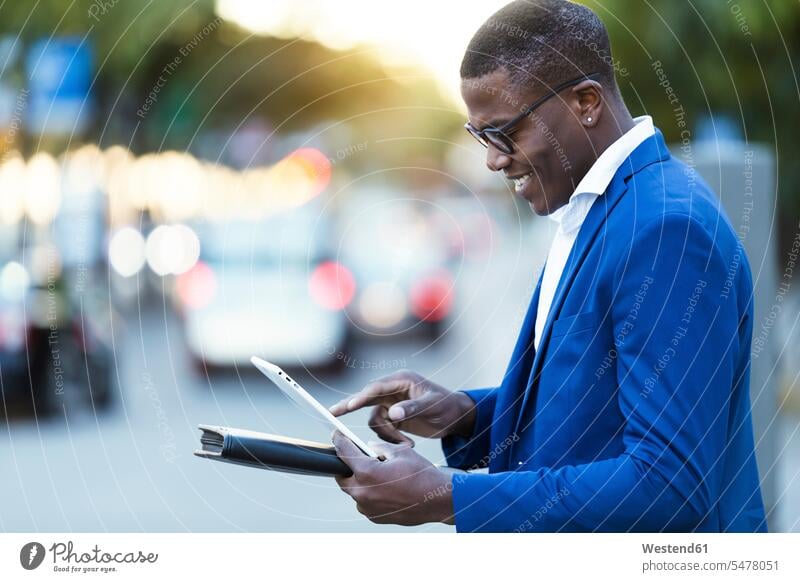 Junger Geschäftsmann in blauer Anzugsjacke und mit seinem digitalen Tablett an einer Straße geschäftlich Geschäftsleben Geschäftswelt Geschäftsperson