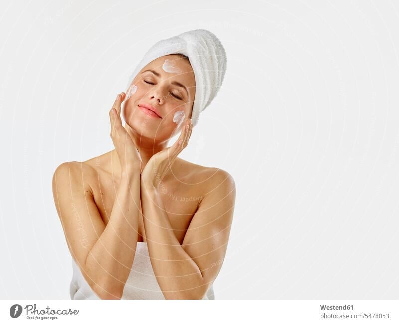Junge Frau trägt Gesichtscreme auf ihr Gesicht auf schön weiblich Frauen Gesichtscremes Hautpflege eincremen Creme Körperpflege Koerperpflege Handtuch