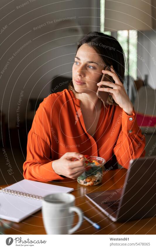 Geschäftsfrau telefoniert mit dem Handy, während sie zu Hause Salat isst Farbaufnahme Farbe Farbfoto Farbphoto Innenaufnahme Innenaufnahmen innen drinnen Tag
