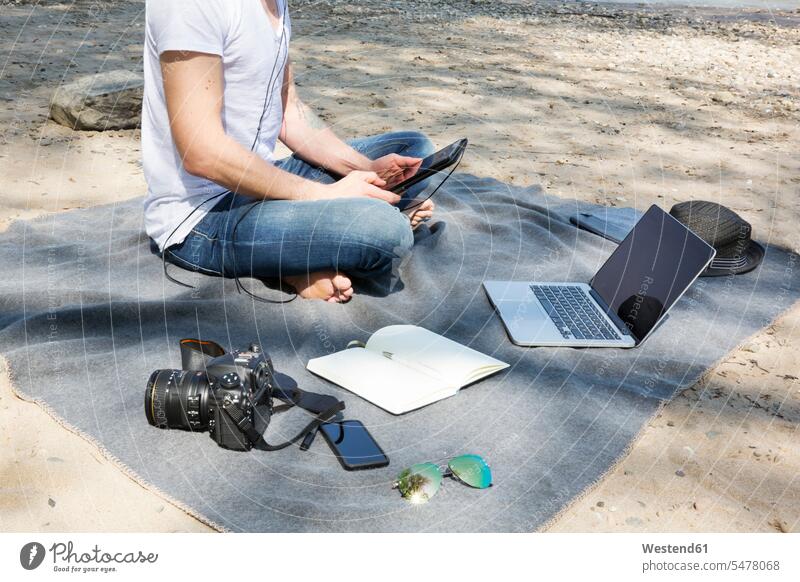 Mann sitzt mit Tablette auf Decke am Strand sitzen sitzend Tablet Computer Tablet-PC Tablet PC iPad Tablet-Computer Männer männlich Decken Beach Straende