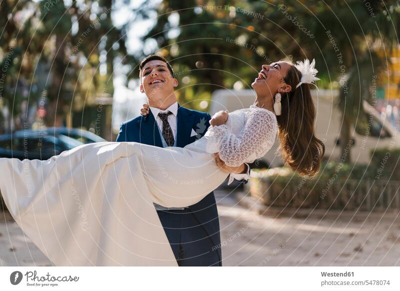 Junger Bräutigam holt fröhliche Braut im Park ab Farbaufnahme Farbe Farbfoto Farbphoto Außenaufnahme außen draußen im Freien Tag Tageslichtaufnahme