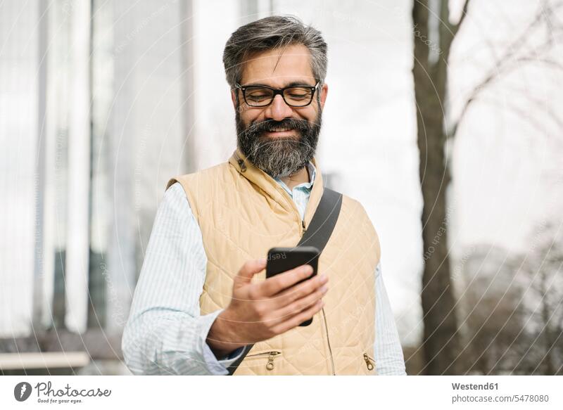 Lächelnder Mann mit Smartphone in der Stadt, Frankfurt, Deutschland geschäftlich Geschäftsleben Geschäftswelt Geschäftsperson Geschäftspersonen Businessmann