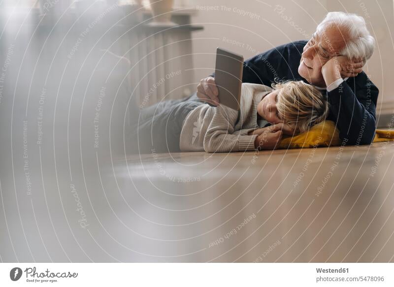 Großvater und Enkel liegen zu Hause mit einer Tablette auf dem Boden Generation Polster Medium Videofilm Videos innig nah liegend liegt daheim Muße Miteinander