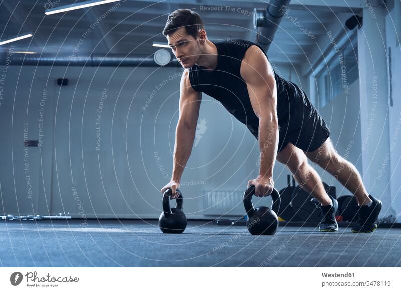 Mann macht Liegestütze auf Kettlebells im Fitnessstudio Workout Übung Uebung Übungen Uebungen Rundgewicht Kugelhantel Fitnessclubs Fitnessstudios Turnhalle