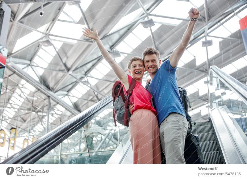 Glückliches Paar jubelt auf Rolltreppe am Flughafen jubeln jauchzen Jubel glücklich glücklich sein glücklichsein Flughaefen Flugplätze Airport Flugplaetze