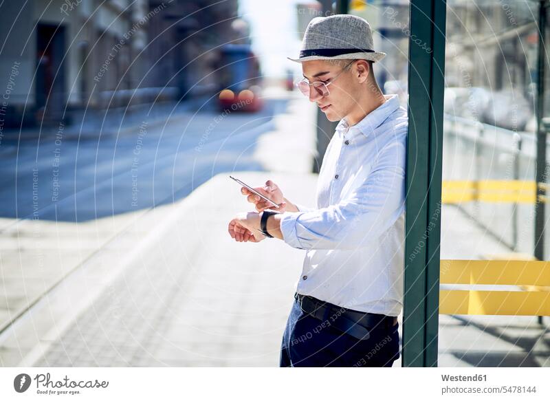 Junger Mann beim Prüfen der Zeit an einer Straßenbahnhaltestelle in der Stadt gemischtrassige Person Haltestelle modisch Termin Termine Drahtlose Technologie