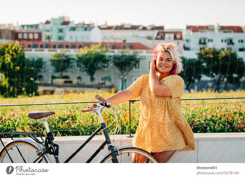 Glückliche übergroße Frau mit Fahrrad am Parkzaun lehnend Farbaufnahme Farbe Farbfoto Farbphoto Außenaufnahme außen draußen im Freien Tag Tageslichtaufnahme