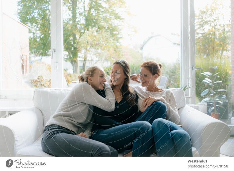 Glückliche Mutter mit zwei Teenager-Mädchen auf der Couch zu Hause Sofa Couches Liege Sofas Teenagerin junges Mädchen Teenagerinnen weiblich junge Frau Tochter