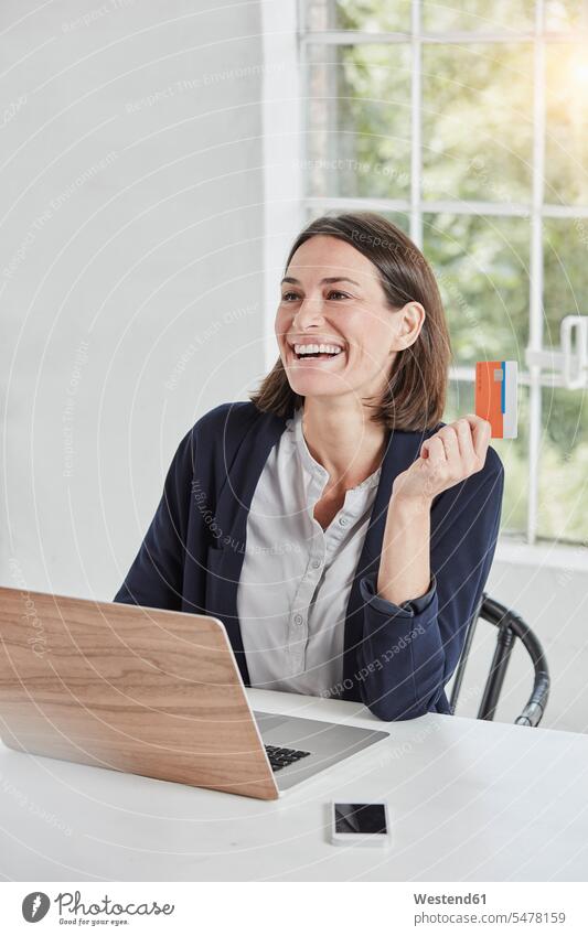 Lachende Geschäftsfrau mit Laptop auf Schreibtisch mit Karte Notebook Laptops Notebooks Arbeitstisch Schreibtische halten Karten lachen Geschäftsfrauen