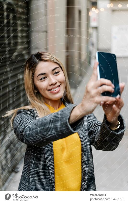 Junge Frau macht Selfie mit ihrem Smartphone in der Stadt Telekommunikation telefonieren Handies Handys Mobiltelefon Mobiltelefone freuen Glück glücklich sein