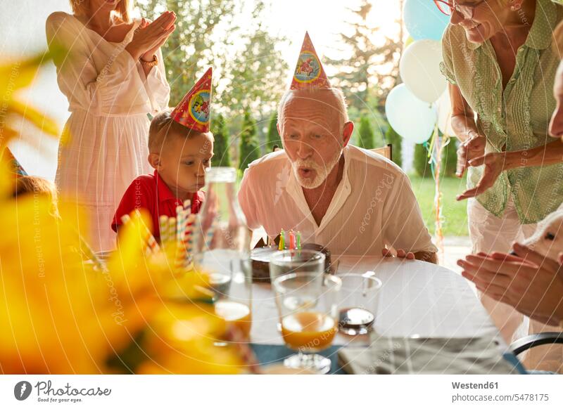 Glückliche Großfamilie beim Ausblasen der Kerzen auf der Geburtstagstorte auf einer Gartenparty Geburtstagsparty Geburtstagspartys Feier Fest Festlichkeit