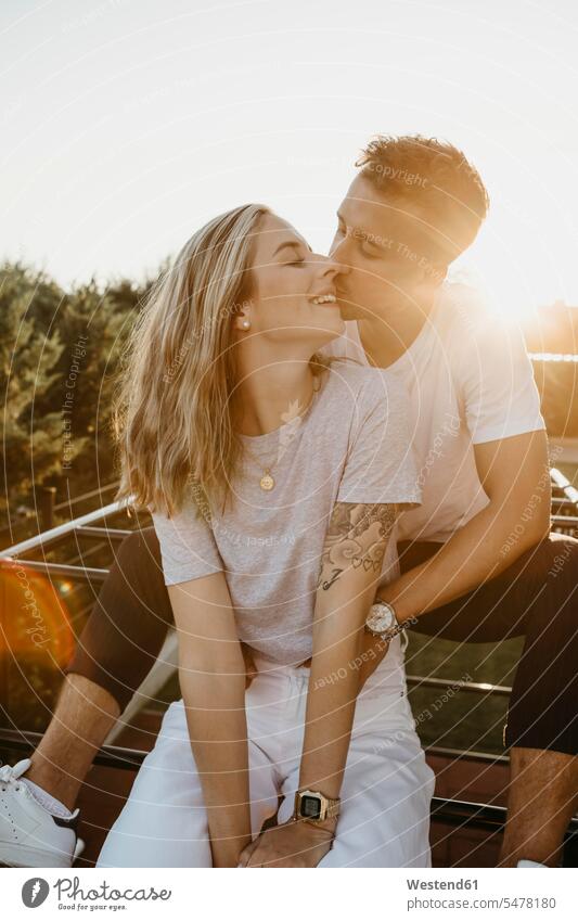 Junges Paar küsst sich bei Sonnenuntergang auf einem Klettergerüst sitzend sitzt Arm umlegen Umarmung Umarmungen abends freuen Glück glücklich sein