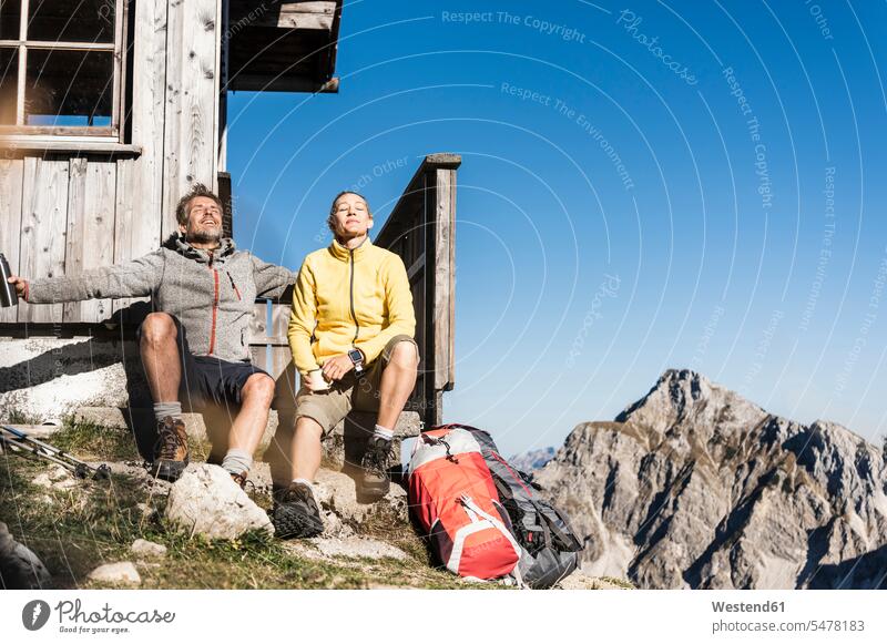 Wanderpärchen vor Berghütte sitzend, eine Pause einlegend ausruhen Rast Erholung erholen Gebirge Berglandschaft Gebirgslandschaft Gebirgskette Gebirgszug Berge