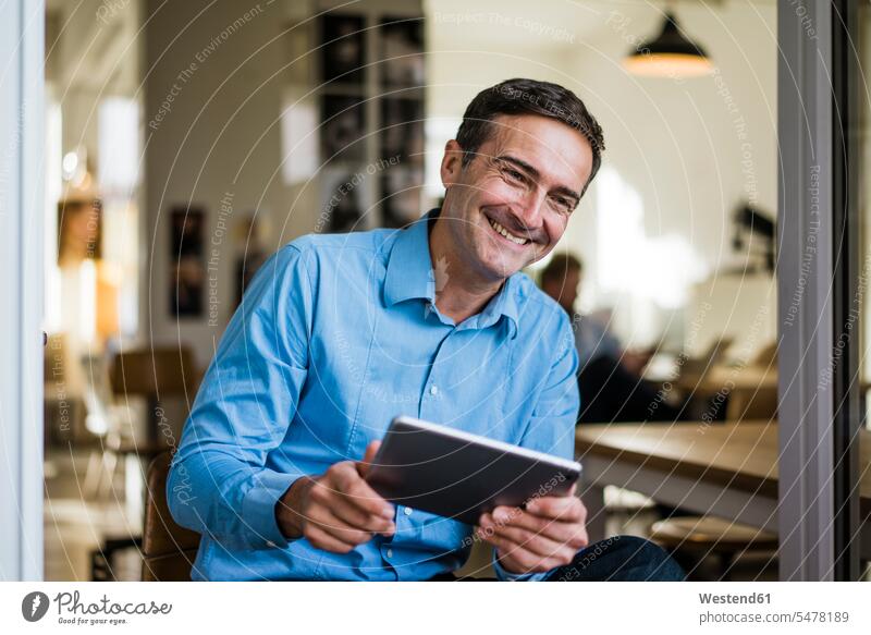 Lächelnder Geschäftsmann mit Tablet sitzt an offener französischer Tür Tablet Computer Tablet-PC Tablet PC iPad Tablet-Computer sitzen sitzend auf geöffnet