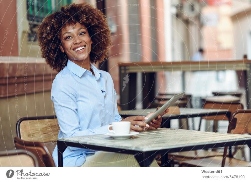 Lächelnde Frau mit Afro-Frisur sitzt im Außencafé mit Tablette weiblich Frauen Afro-Look Afros Afrolook Tablet Computer Tablet-PC Tablet PC iPad Tablet-Computer