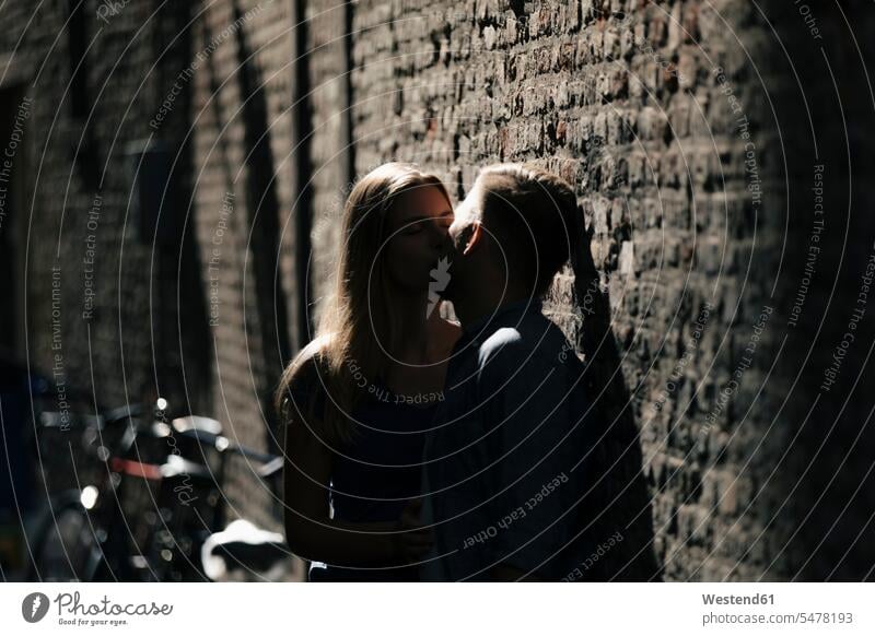 Zärtliches junges Paar küsst sich an der Backsteinmauer Backsteinwand Backsteinmauern küssen Küsse Kuss Zuneigung Pärchen Paare Partnerschaft Ziegelmauer