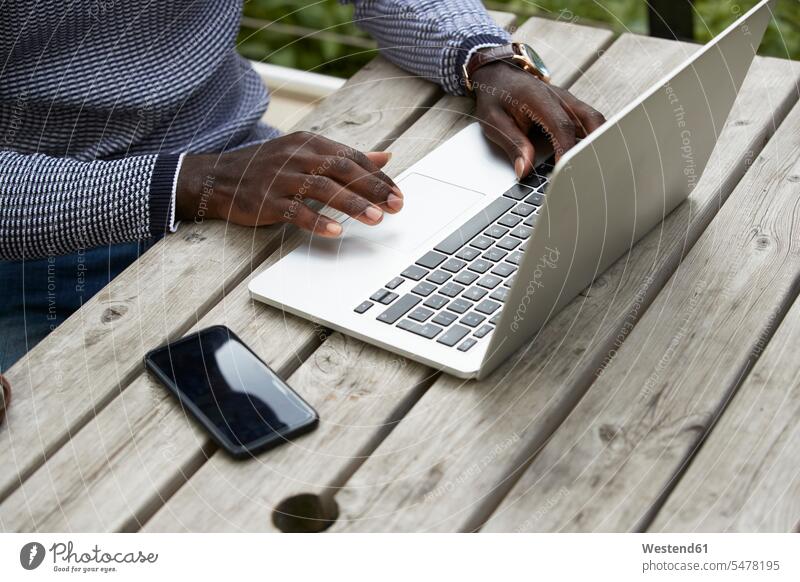 Männlicher Profi benutzt Laptop am Holztisch Farbaufnahme Farbe Farbfoto Farbphoto Außenaufnahme außen draußen im Freien Tag Tageslichtaufnahme