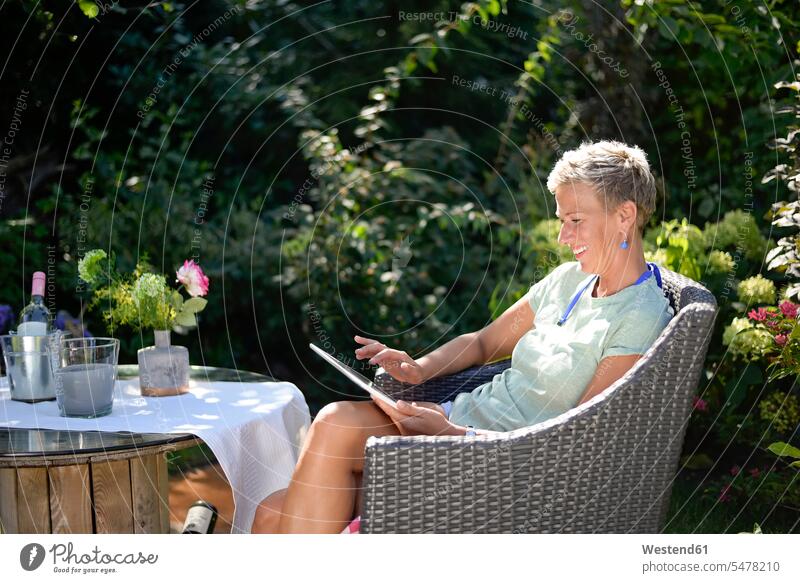 Lächelnde Frau sitzt im Garten und benutzt ein digitales Tablet lächeln sitzen sitzend weiblich Frauen Gärten Gaerten Tablet Computer Tablet-PC Tablet PC iPad