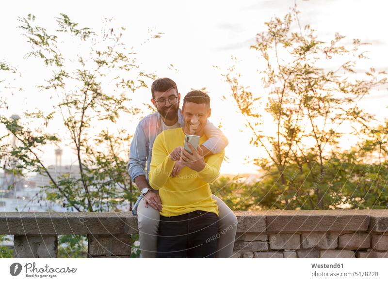 Homosexuelles Paar telefoniert bei Sonnenuntergang im Freien Partner Partnerschaften Telekommunikation telefonieren Handies Handys Mobiltelefon Mobiltelefone