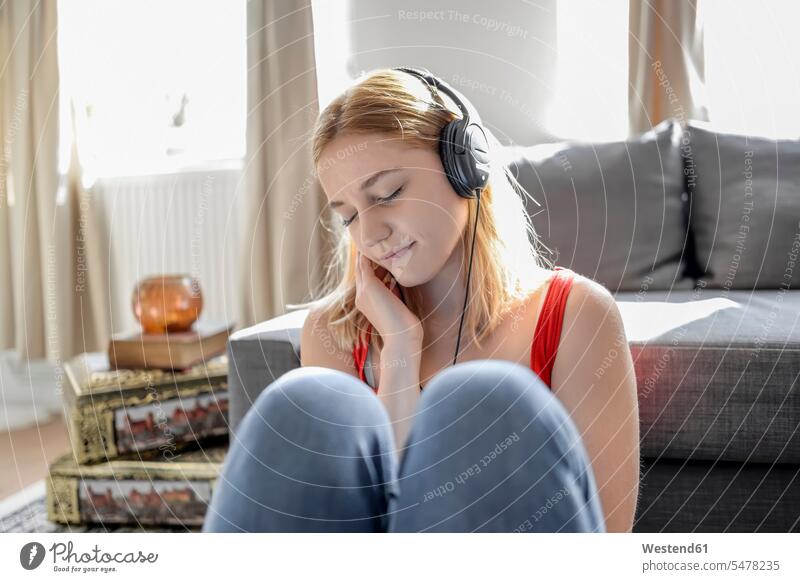 Porträt einer jungen Frau mit geschlossenen Augen, die zu Hause auf dem Boden sitzt und mit Kopfhörern Musik hört Leute Menschen People Person Personen