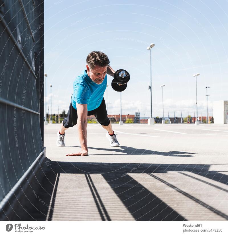 Mann trainiert mit Hanteln, macht einarmige Planke Kraft stark Stärke kräftig Gewicht Gewichte trainieren Workout Liegestützen Push-Up Pushups Push-Ups