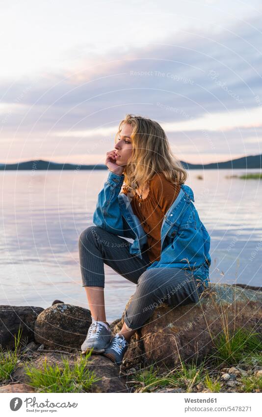 Finnland, Lappland, junge Frau sitzt auf einem Felsen am Seeufer Seen Landschaft Landschaften weiblich Frauen sitzen sitzend Gewässer Wasser Gestein Steine
