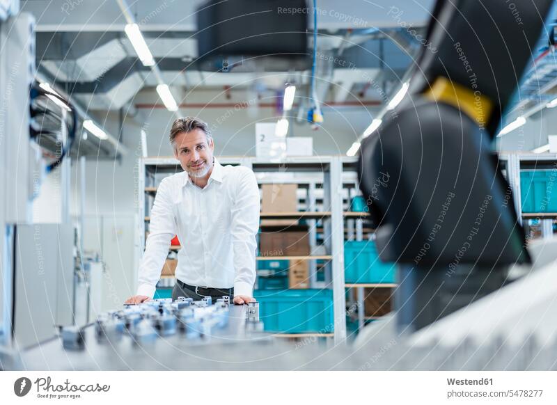 Selbstbewusster Geschäftsmann in einer modernen Fabrikhalle mit Blick auf Roboter Job Berufe Berufstätigkeit Beschäftigung Jobs geschäftlich Geschäftsleben