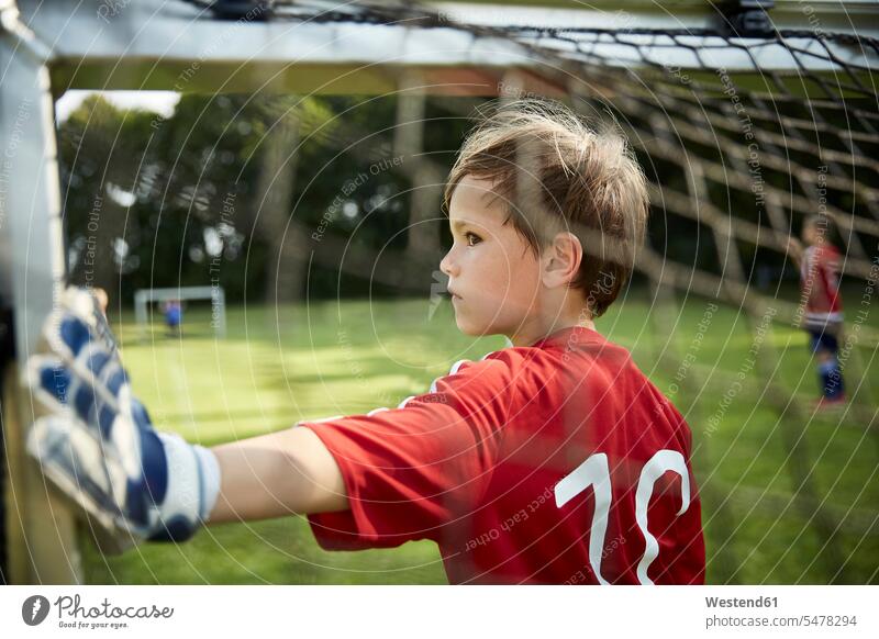 Seriöser Junge in Fussballuniform hält Torpfosten auf dem Feld Farbaufnahme Farbe Farbfoto Farbphoto Außenaufnahme außen draußen im Freien Tag