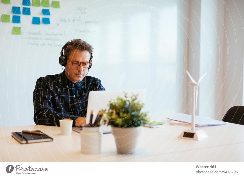Geschäftsmann trägt Kopfhörer mit Laptop am Schreibtisch im Büro Businessmann Businessmänner Geschäftsmänner Office Büros Arbeitstisch Schreibtische Notebook