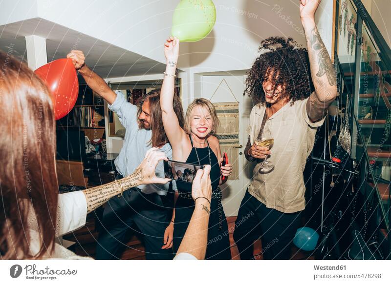 Frau fotografiert glückliche Freunde beim Tanzen während eines geselligen Beisammenseins zu Hause Farbaufnahme Farbe Farbfoto Farbphoto Innenaufnahme