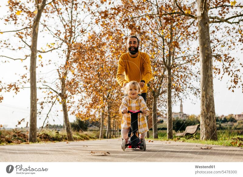 Vater und Tochter genießen einen Morgen Tag im Park im Herbst, Mädchen auf Roller herbstlich Parkanlagen Parks Dreirad Dreiraeder Dreiräder Papas Väter Vati