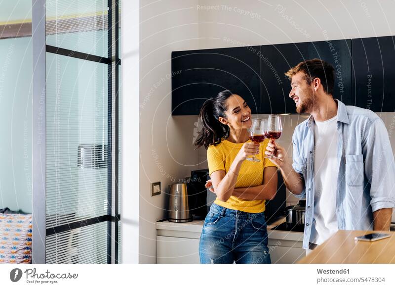 Glückliches junges Paar trinkt zu Hause gemeinsam Wein in der Küche Gläser Trinkglas Trinkgläser Weingläser freuen Frohsinn Fröhlichkeit Heiterkeit geniessen