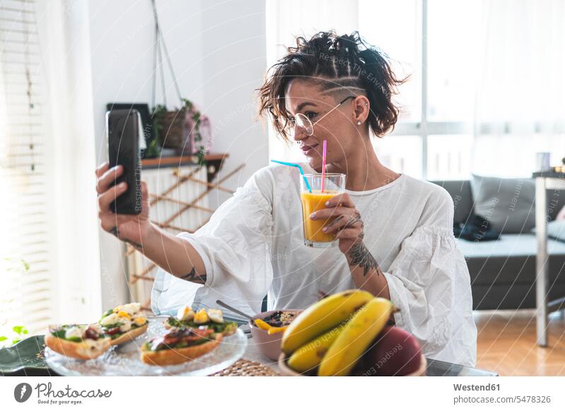 Porträt einer jungen Frau, die ein Selfie mit ihrem Smartphone macht, während sie frühstückt Innenaufnahme Innenaufnahmen innen drinnen Tag Tageslichtaufnahme