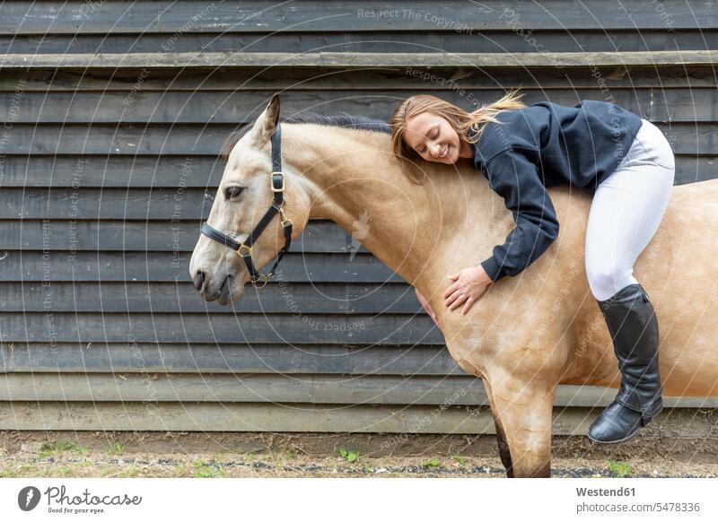 Junge Frau auf dem Rücken ihres Pferdes liegend lachen offenes Laecheln selbstbewusst Selbstvertrauen Vertrauen Zuversichtlich Leute Menschen People Person