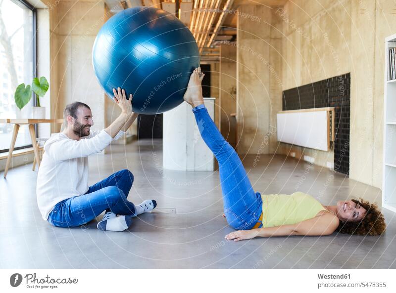 Glücklicher Mann und Frau üben mit Fitness-Ball in modernen Büro Deutschland Freiberufler freiberuflich freie Berufe Angestellte Mitarbeiterin Kollegin
