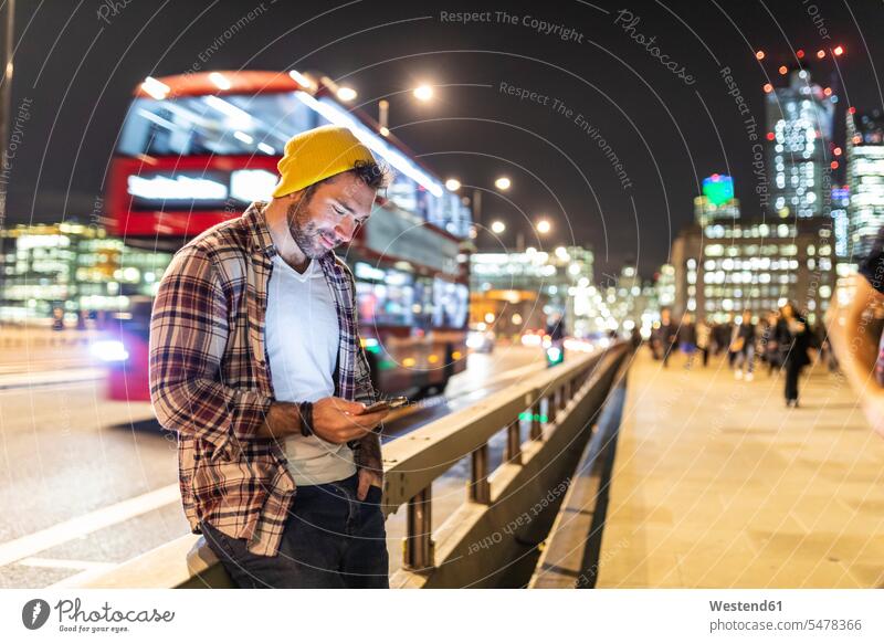 UK, London, lächelnd Mann mit Telefon auf der Straße in der Stadt in der Nacht nachts staedtisch städtisch Handy Mobiltelefon Handies Handys Mobiltelefone