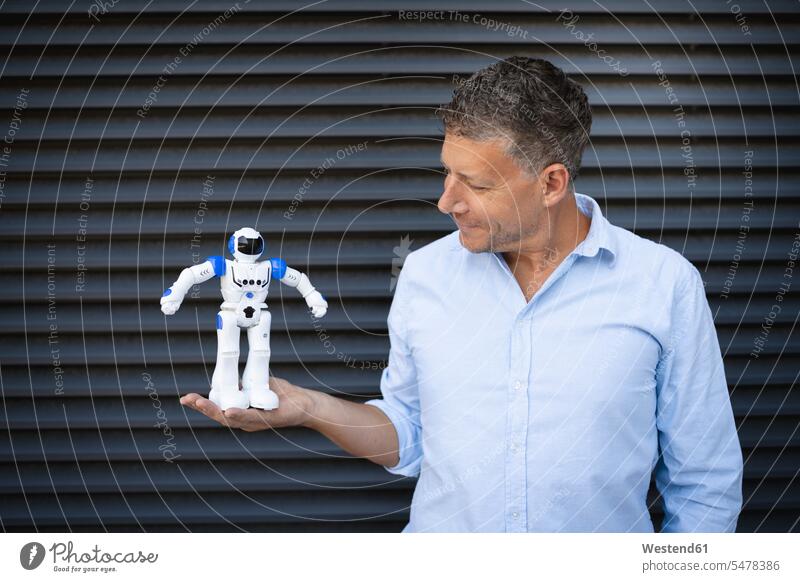 Geschäftsmann hält Roboter, während er an einer Metallwand steht Farbaufnahme Farbe Farbfoto Farbphoto Außenaufnahme außen draußen im Freien Tag