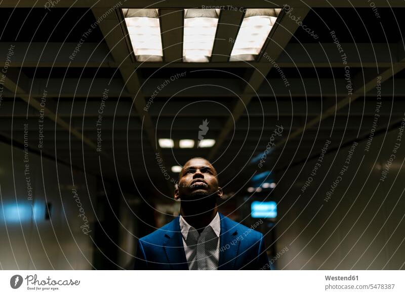Männlicher Unternehmer schaut auf, während er unter beleuchtetem Licht in der U-Bahn steht Farbaufnahme Farbe Farbfoto Farbphoto Spanien Geschäftsmann
