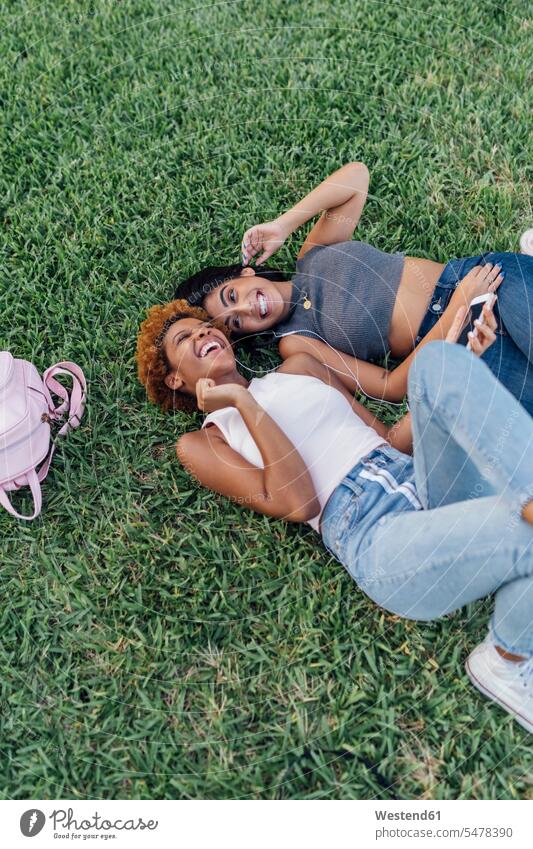 Zwei glückliche Freundinnen entspannen sich in einem Park und hören Musik hoeren Glück glücklich sein glücklichsein entspannt entspanntheit relaxt Parkanlagen