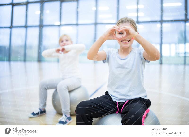 Porträt von lächelnden Schulmädchen, die im Sportunterricht auf Turnbällen sitzen Fitnessball Portrait Schülerin Schule Schulkind Bildung Unterricht positiv