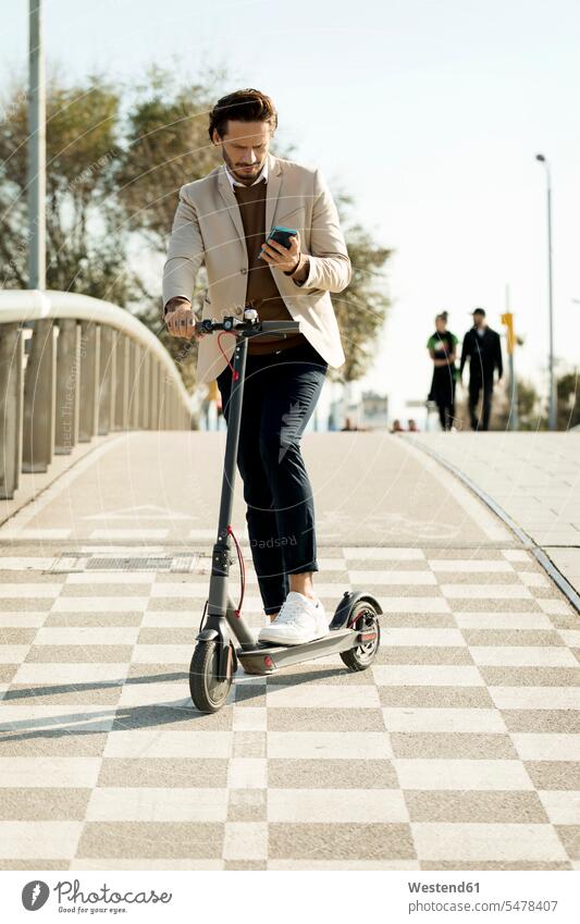 Mann mit E-Scooter und Mobiltelefon in der Stadt, Teilansicht Männer männlich ansehen Roller Smartphone iPhone Smartphones Elektroroller staedtisch städtisch