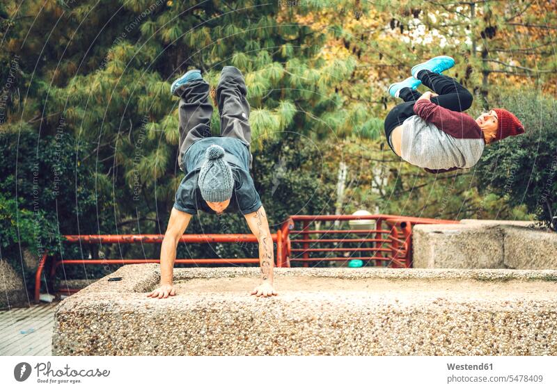 Junger Mann macht Handstand, während Freund im Park springt Herbst Jahreszeit Jahreszeiten Freizeitkleidung Freizeitbekleidung casual Farbaufnahme Farbe