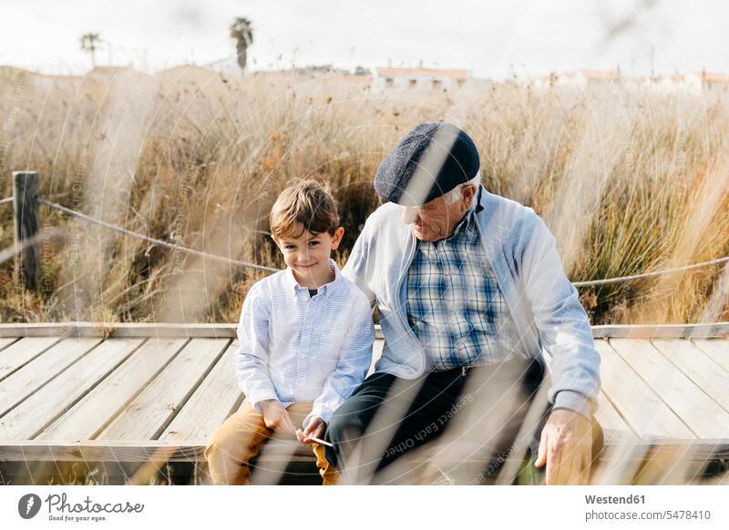 Großvater sitzt mit seinem Enkel auf der Strandpromenade und entspannt sich Europäer Kaukasier Europäisch kaukasisch Gemeinsamkeit zusammen gemeinsam