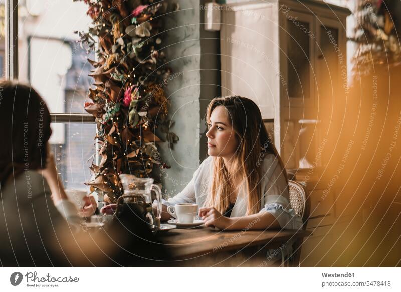 Zwei junge Frauen sitzen am Tisch in einem Cafe Freundinnen nachdenken überlegen dekoriert Verträumt träumerisch Betrachtung Nachsinnen betrachten Kontemplation
