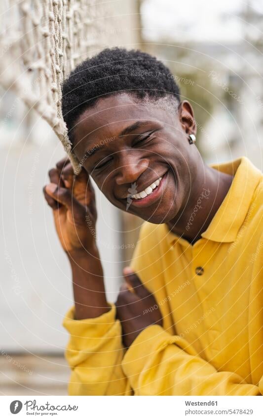 Porträt eines jungen schwarzen Mannes, der am Volleyballnetz steht und lacht Schwarzer Afrikanisch Farbige Afrikanische Abstammung dunkelhäutig Farbiger